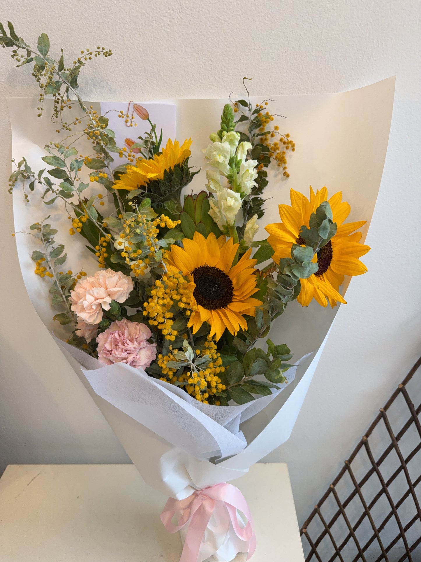 Bouquet of sunflowers and other flowers wrapped in white paper finished with Satin Ribbon.