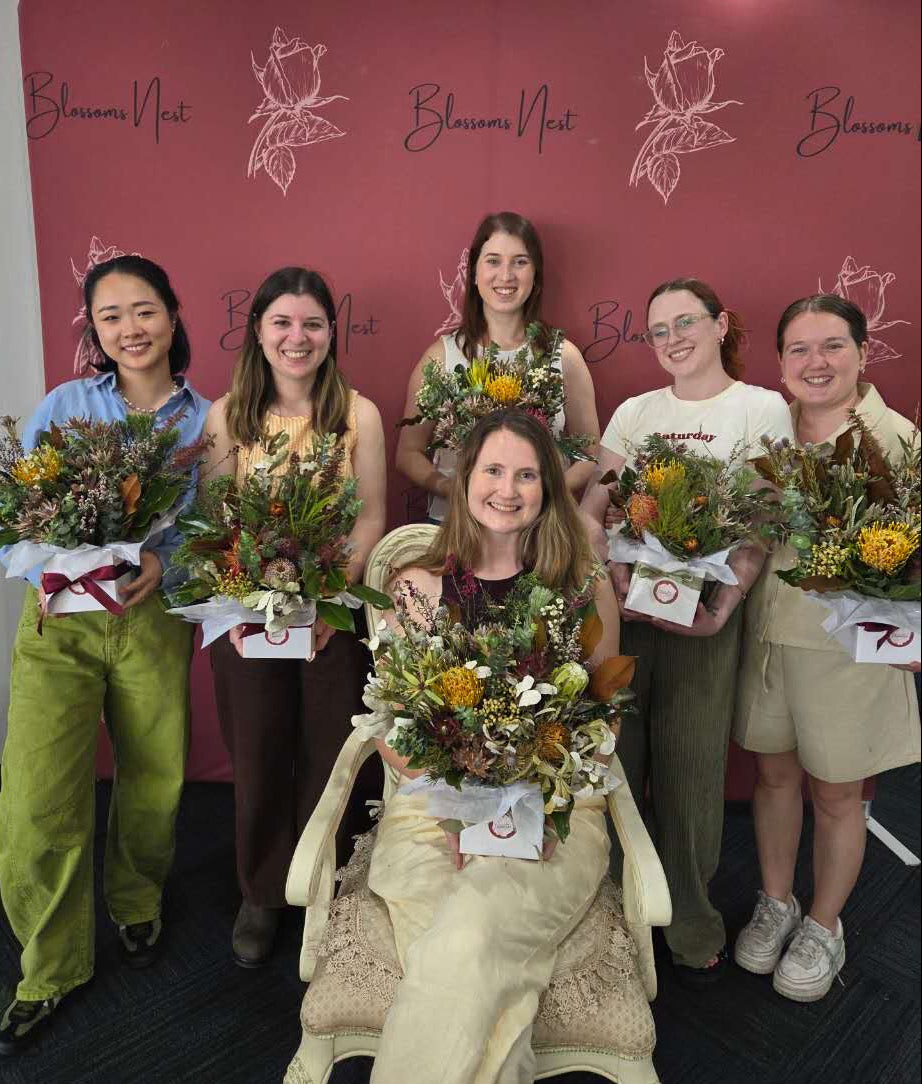 Group of people holding floral arrangements in front of a 'Blumen Nest' branded wall.